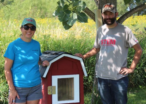 Normal Community High School teacher, Daniel Higby (right) and ISU Horticulture Center Coordinator, Jessica Chambers show off the new Little Free Library constructed by students and sponsored by McLean County Farm Bureau